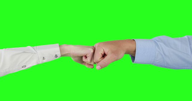 Two individuals of diverse ethnicities are engaging in a fist bump, with copy space on a green background. This gesture often signifies agreement, camaraderie, or a casual greeting between people.