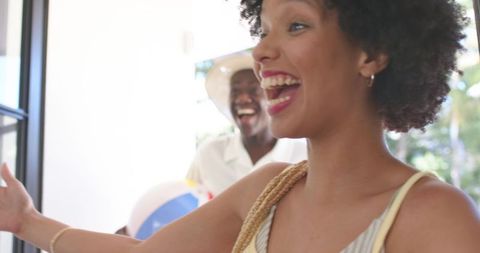 African american friends greeting at home doorway laughing with beach ball