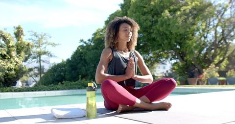 Woman Meditating in Lotus Pose by Poolside on a Sunny Day