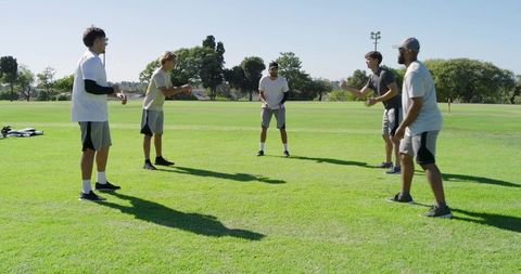 Diverse young men warming up for team training on sunlit park field athletic teamwork
