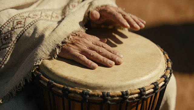 Senior hands playing djembe outdoors tapping rope-tuned drum skin for rhythmic music