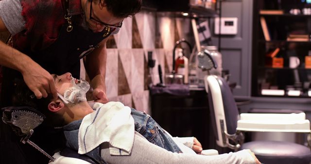 Barber carefully shaving customer reclining in chair, creating a relaxed and comfortable environment. Useful for depicting grooming services, men's beauty routines, professional barber skills, or the ambiance of a modern barbershop.