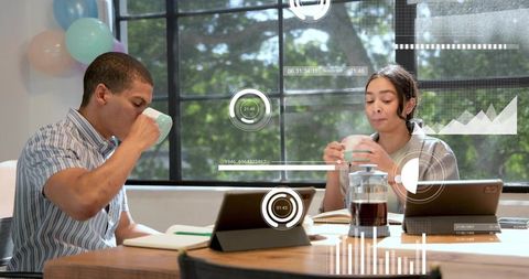 Coworking duo sipping coffee collaborating with augmented reality dashboards on tablets