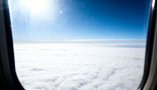 Soaring above endless cloud layer through airplane window with bright sun glare