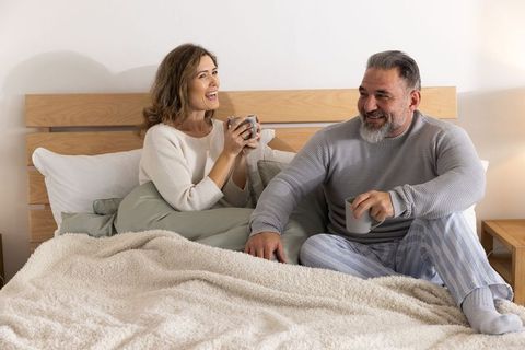 Middle-aged couple enjoying cozy morning coffee in bed relaxed intimate moment