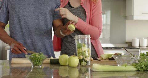 Couple preparing green smoothie at kitchen island chopping apples and leafy greens