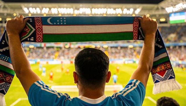 Adult male raising uzbekistan scarf overhead cheering football fan in night stadium