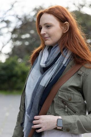 Redhead woman wearing olive jacket and striped scarf checking smartwatch on outdoor walk