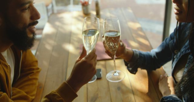Biracial couple are toasting with champagne, celebrating. He has beard, wearing a yellow jacket; she has curly hair, in a denim jacket