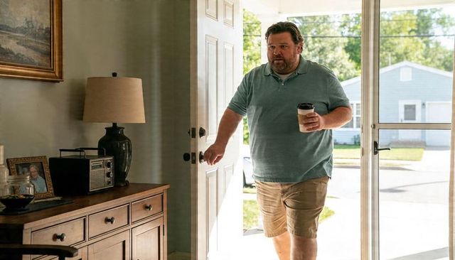 Casual man entering home holding coffee through open front door on sunny suburban morning
