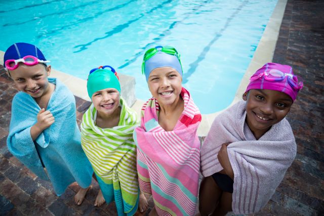 Portrait of little swimmers wrapped in towels standing at poolside