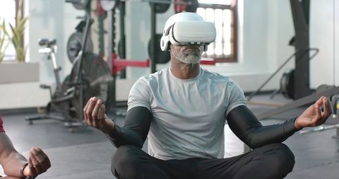 African american man meditating in gym wearing white vr headset for mindful fitness