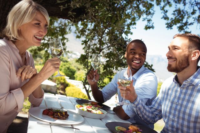 Group of friends enjoying a meal and champagne outdoors at a restaurant. Ideal for use in content related to social gatherings, celebrations, dining experiences, and lifestyle. Perfect for promoting restaurants, outdoor events, and social activities.
