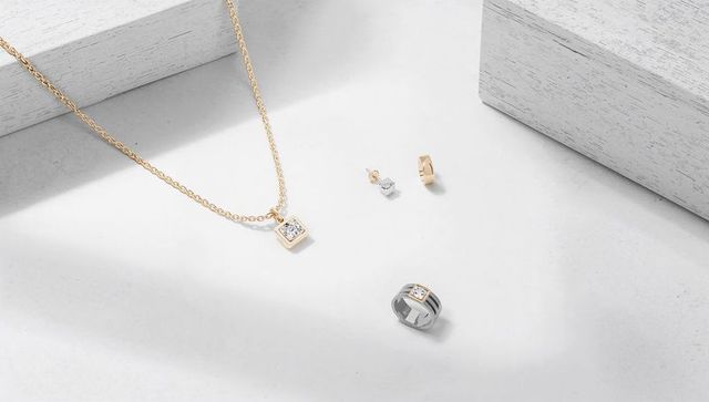 Minimalist gold pendant necklace featuring stud earrings and modern silver ring on cream surface