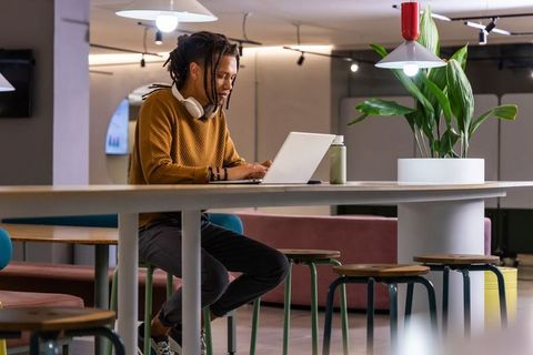 African american man working on laptop in modern coworking lounge, wearing headphones