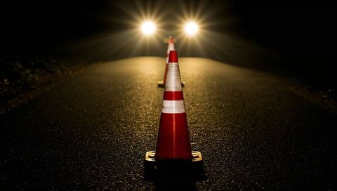 Backlit traffic cones aligning lane on dark road guiding drivers toward headlights