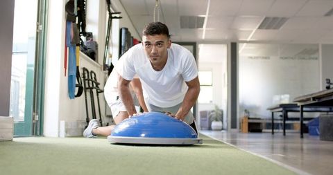 Focused man performing push-ups on balance trainer in rehabilitation center