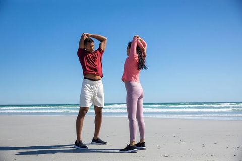 Friends stretching on sunny beach in sportswear by ocean