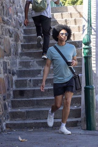 African american man walking down sunlit stone steps holding to-go coffee wearing sunglasses