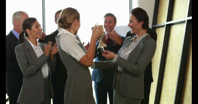 A group of diverse professionals celebrates a success, with a woman holding a trophy and others applauding her achievement. The joyous atmosphere suggests a team recognizing a colleague's accomplishment, fostering a culture of appreciation and motivation.