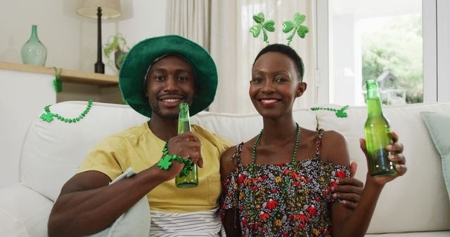 Portrait of african american couple in st patrick's day hats holding beers smiling to camera. staying at home in isolation during quarantine lockdown.
