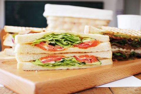 Stacking fresh tomato and lettuce sandwich on white bread on wooden board for lunch