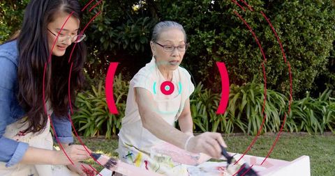 Intergenerational women painting wooden box together in backyard garden with pastel tones