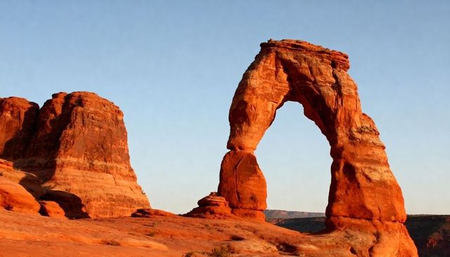 Sunlit red sandstone arch rising over desert plateau at golden hour, weathered rock