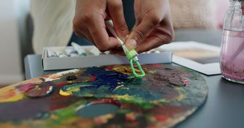 Female hands squeezing green acrylic paint onto wooden palette for color mixing