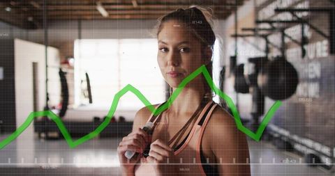 Fit woman holding jump rope in industrial gym with green analytics graph overlay