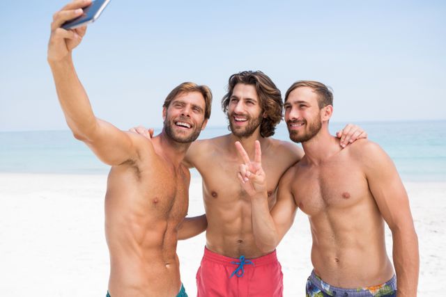 Smiling male friends taking selfie while standing at beach on sunny day