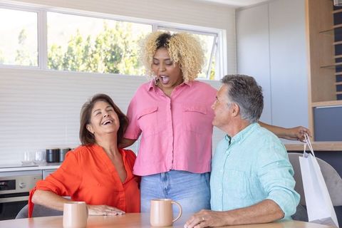 Multigenerational diverse family hugging and laughing around kitchen table