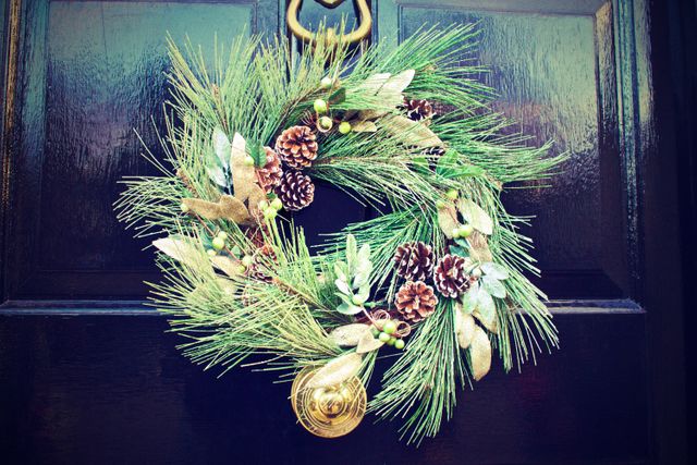 Traditional Christmas wreath featuring pinecones, greenery, and golden accents hanging on front door. Perfect for use in holiday greeting cards, festive promotion materials, or decorating inspiration.