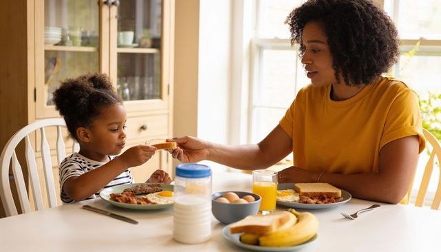 Mother and daughter sharing breakfast toast at sunlit kitchen table, cozy family morning