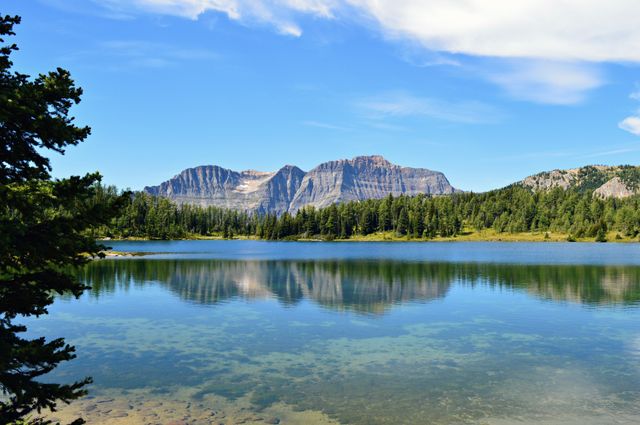 Featuring serene mountain lake reflecting surrounding forests and blue sky, ideal for travel websites, outdoor magazines, and nature blogs. Suitable for promoting camping, hiking, and scenic destinations.