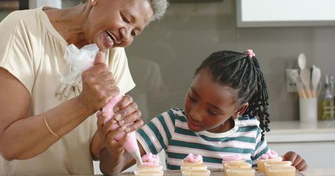 African american grandmother and granddaughter decorating cupcakes with pink frosting