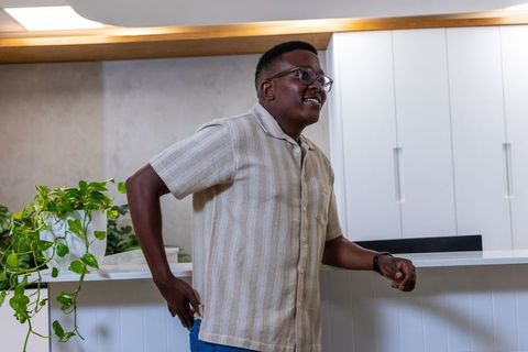 African american man leaning on white counter smiling in modern reception lounge with greenery