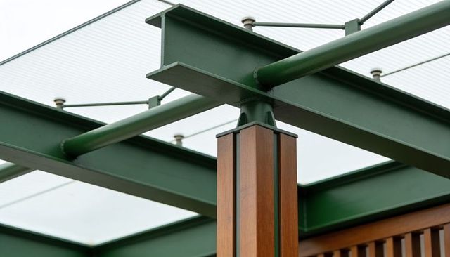 Green steel beam connecting wood-clad post at modern pergola canopy