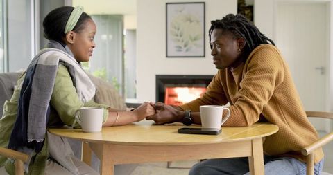 African American couple holding hands at cozy round table by fireplace, intimate moment