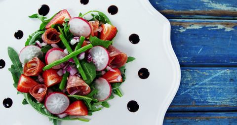 Exquisite and colorful salad featuring fresh arugula curl around sliced strawberries, topped with crisp radishes and served with curled prosciutto. Ideal for illustrating healthy lifestyle and culinary excellence concepts or menus for fine dining establishments or food blogs.