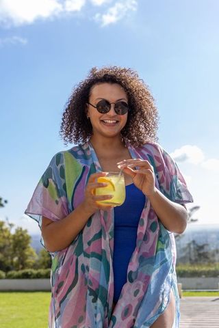 African american woman enjoying summer lemonade on sunny terrace wearing vibrant cover-up