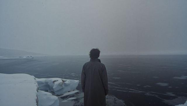 Solitary figure standing on icy cliff overlooking frozen sea at foggy arctic horizon