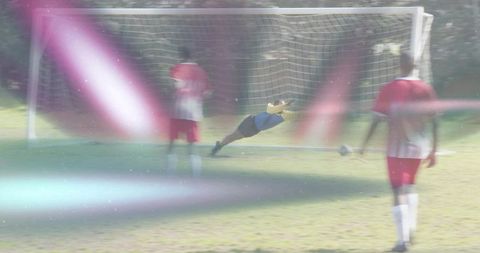 Diving goalkeeper making spectacular save with motion blur and lens flare on grass pitch