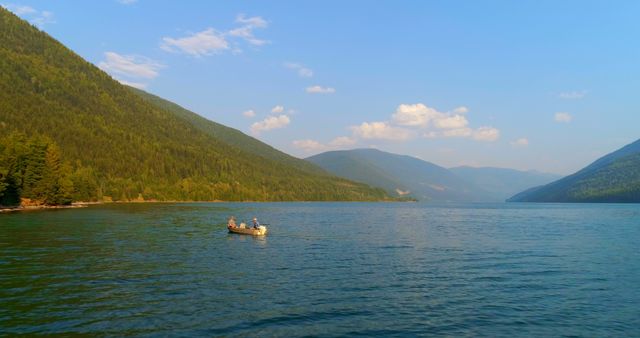 A small boat with several individuals is floating on a vast lake surrounded by mountains, with copy space. The serene landscape suggests a peaceful boating excursion in a picturesque natural setting.