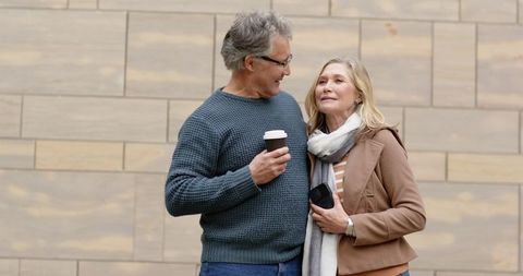 Mature couple enjoying coffee walk, embracing warmth and conversation in urban stroll