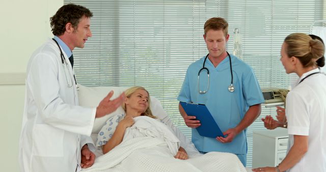 A diverse group of healthcare professionals, including Caucasian and Biracial doctors and nurses, are attending to a patient in a hospital room, with copy space. They are engaged in a discussion about the patient's care, indicating a collaborative medical environment.