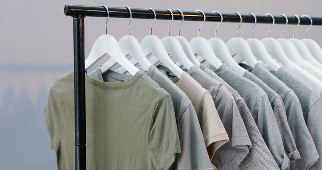A selection of plain t-shirts in neutral colors is neatly organized on white hangers, with copy space. The arrangement suggests a minimalist wardrobe or a retail clothing display.