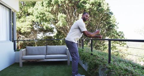 Man leaning on balcony railing holding smartphone overlooking lush green landscape
