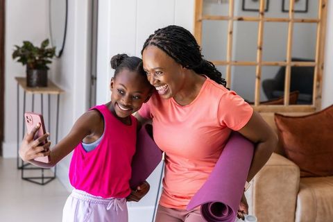 African mother and daughter taking selfie after home yoga session, smiling, fitness bonding