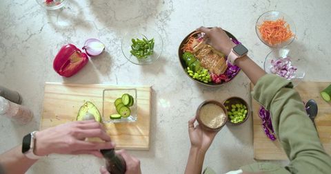 Couple assembling vibrant grain bowls with tofu, edamame, avocado and sesame
